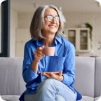 Woman sits on her couch holding a mug of coffee.